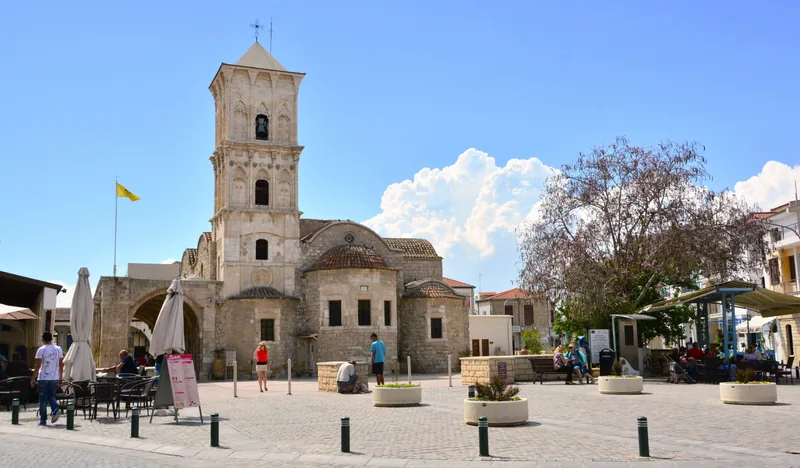 The church of Saint Lazarus in Larnaca, a stone bell tower over a domed church, with café tables on the square in front.