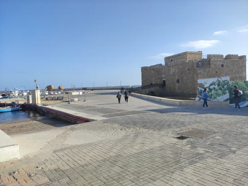 Paphos harbour: a wide paved quay leading to the squat stone fort at the end of the breakwater, under a clear sky.